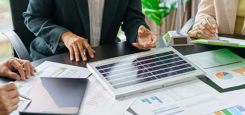 scrivania di un ufficio con persone al lavoro su tablet e grafici, intente a individuare le soluzioni migliori per aumentare il risparmio energetico dell'azienda