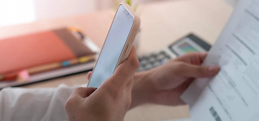 mano di un uomo che esamina i documenti con la voltura mentre controlla i passaggi da fare sul proprio smartphone