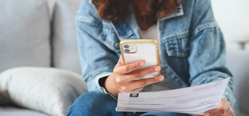 donna che esamina i documenti per la voltura luce e gas, mentre controlla sullo smartphone qual è la documentazione necessaria